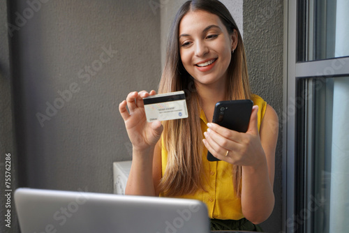 Pretty girl holding credit card and using smartphone at home. Businesswoman shopping online, e-commerce, internet banking, working from home concept. photo