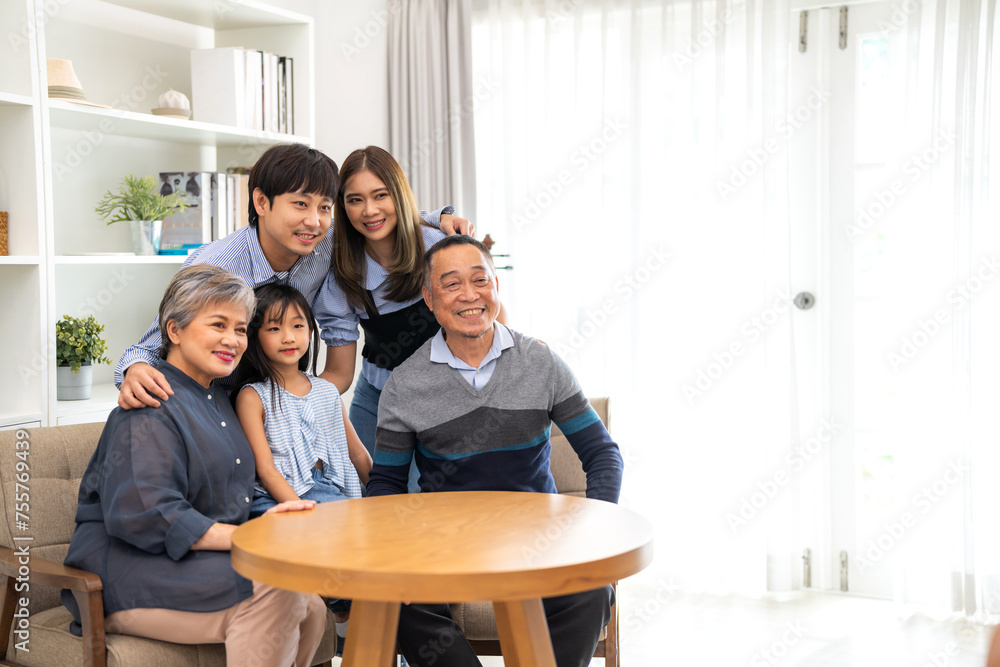 A family of five, including a grandfather and his grandchildren, are sitting around a wooden table in a living room. Scene is warm and loving, as the family members are posing for a photo together A family of five, including a grandfather and his grandchildren, are sitting around a wooden table in a living room. Scene is warm and loving, as the family members are posing for a photo together