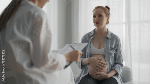 Pregnant woman consulting with a doctor. Smiling young pregnant woman patient answers gynecologist questions at hospital, medical clinic. Doctor examine pregnant belly check up. Gynecology concept. photo