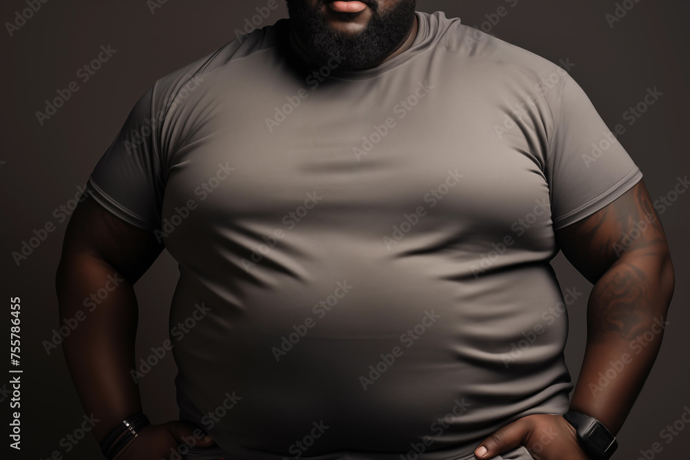 Close-up of a confident, plus-sized man in a gray t-shirt, with a dark background enhancing his strong posture