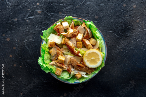Caesar salad with chicken breast, lettuce, croutons, and a lemon, overhead flat lay shot on a slate background
