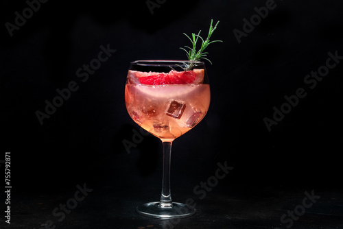 Fancy cocktail with fresh fruit. Gin and tonic drink with ice at a party, on a black background. Alcohol with pink grapefuit and rosemary