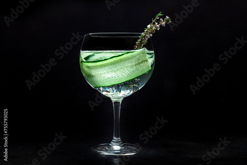 Fancy fresh cocktail. Gin and tonic drink with ice at a party, on a black background. Alcohol with cucumber and thyme