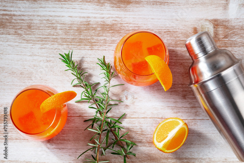 Orange cocktails with rosemary and a shaker, overhead flat lay shot on a wooden background
