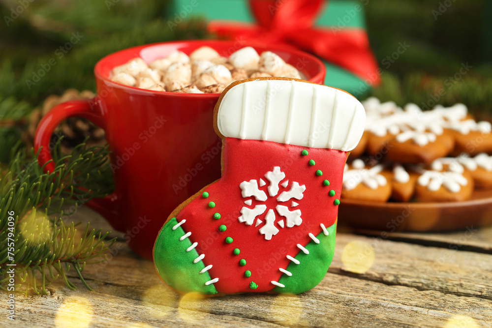 Tasty cookie in shape of Christmas stocking, cocoa with marshmallows and fir tree branch on wooden table, closeup. Space for text