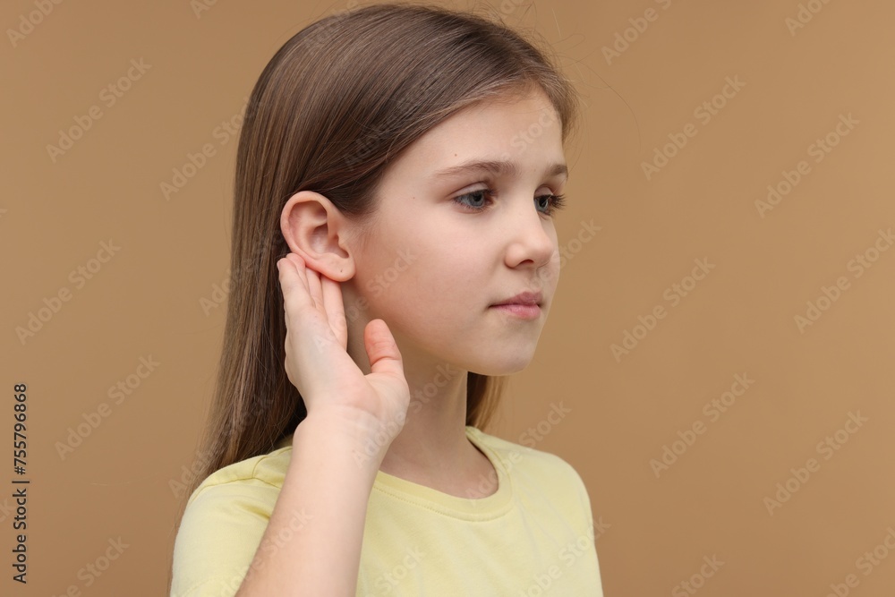 Little girl with hearing problem on pale brown background, space for text Little girl with hearing problem on pale brown background, space for text