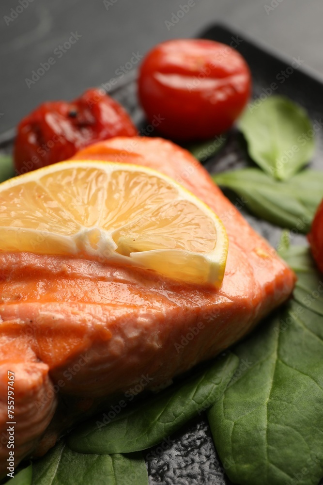 Tasty grilled salmon with lemon, spinach and tomatoes on table, closeup