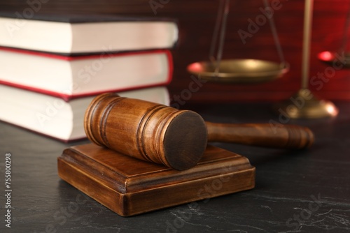 Wooden gavel, scales and stack of books on dark textured table, closeup