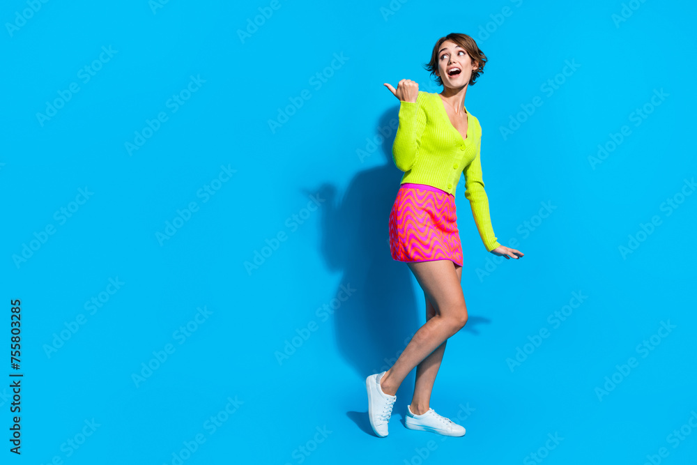 Full length photo of charming gorgeous adorable lady in summer outfit slender fit point finger billboard isolated on blue color background Full length photo of charming gorgeous adorable lady in summer outfit slender fit point finger billboard isolated on blue color background