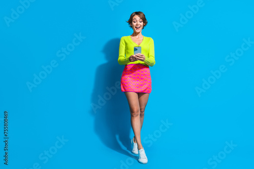 Full body size photo of amazed young lady in shirt mini skirt using smartphone found nice deal aliexpress isolated on blue color background
