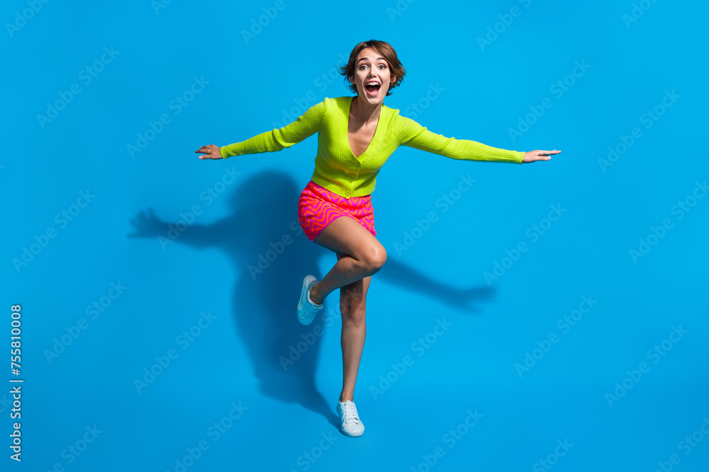 Full length body photo of charming lady dressed green cardigan with pink mini skirt flying forward isolated on blue color background