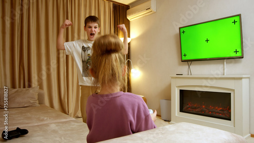 Children in a home interior enjoying playing a game console against a green TV screen background. Game console, video games, technology, recreation.