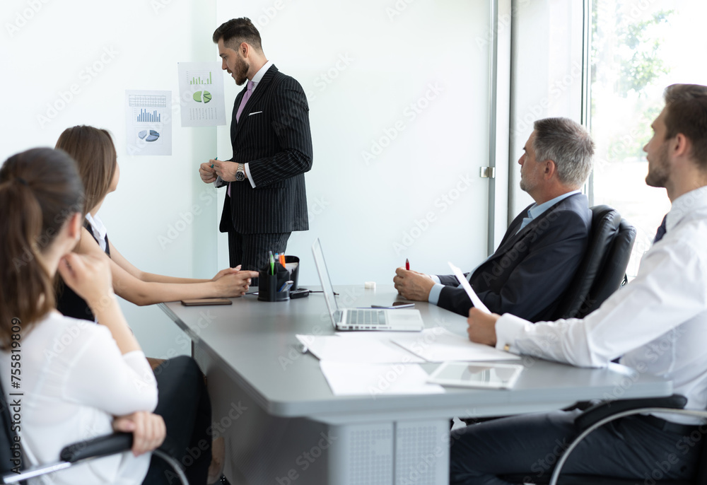 Business man presenter team leader wearing suit giving presentation training on whiteboard in office. Male company executive manager presenting corporate strategy at group conference meeting