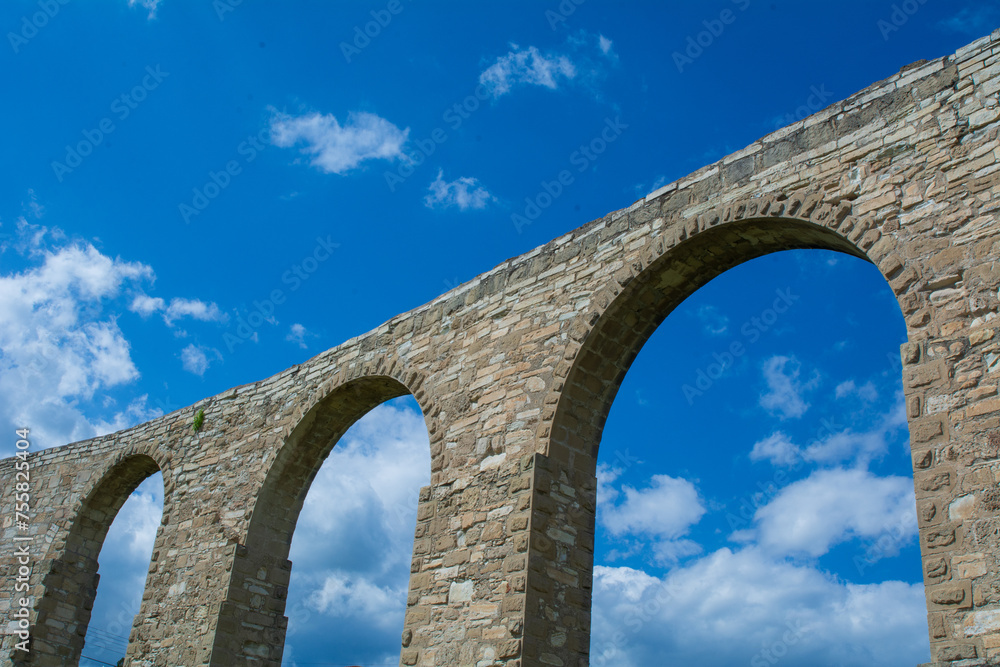 low-angle view of an ancient aqueduct against a blue sky