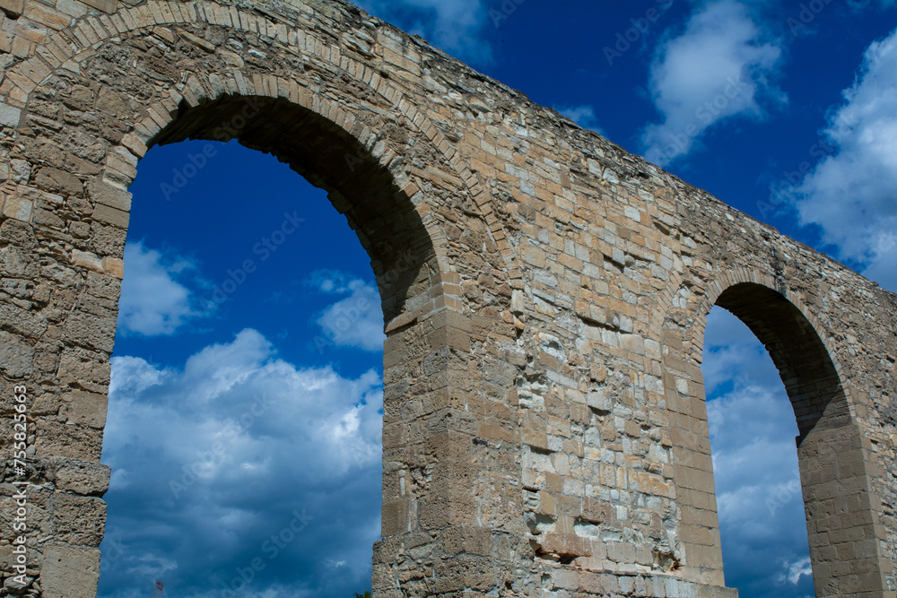 low-angle view of an ancient aqueduct against a blue sky