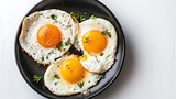 Fried eggs with parsley on black plate over white background.