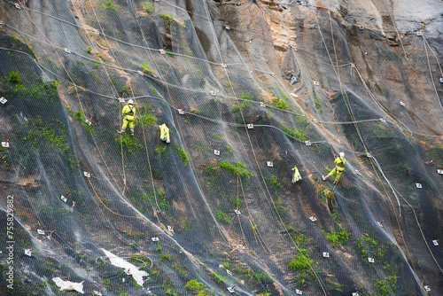 Workers strengthen the slope of the mountain with a metal mesh preventing rockfall on the road. Hondarribia, Spain. Abstract safety concept background.