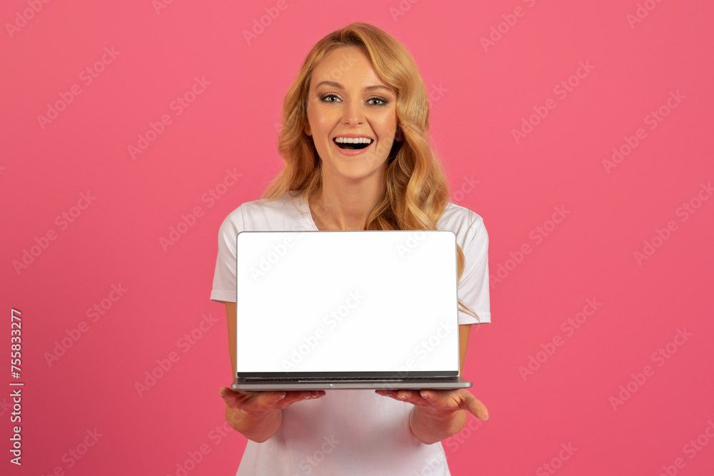 Naklejka premium Happy blonde woman holds laptop showcasing computer blank screen, studio