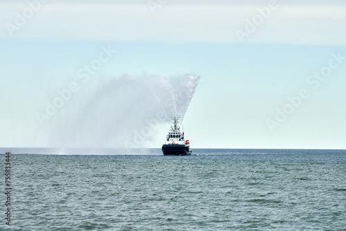 Fireboat ship sails on open sea directing jets of water to sides demonstrating bravery water salute, nautical spectacle of russian maritime strength at Russian naval forces parade