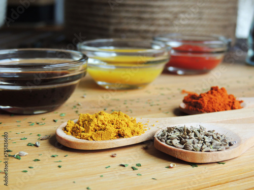 Fototapeta Naklejka Na Ścianę i Meble -  On a wooden cutting board, several wooden spoons with colorful spices such as turmeric, paprika, paprika, and cumin with various sauces in a glass jar at the bottom.