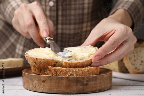 Woman spreading butter onto bread at white wooden table, closeup