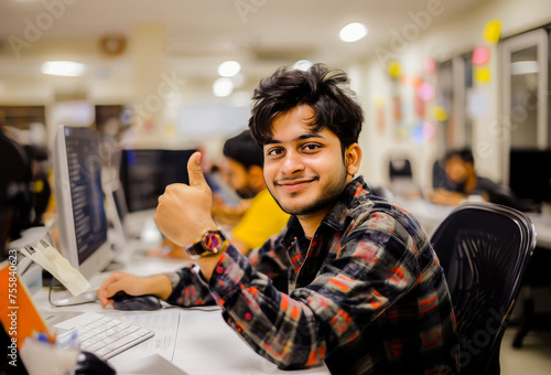 A cheerful young man giving a thumbs up at his office computer, displaying satisfaction with his work. photo