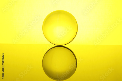 Transparent glass ball on mirror surface against yellow background