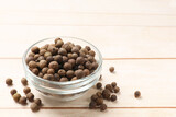 Dry allspice berries (Jamaica pepper) in bowl on light wooden table, space for text