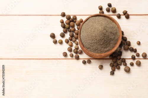 Ground and whole allspice berries (Jamaica pepper) in bowl on light wooden table, top view. Space for text