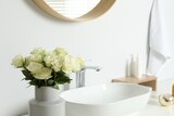 Vase with beautiful white roses near sink in bathroom