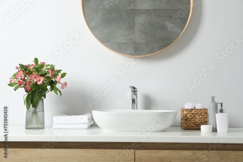 Vase with beautiful Alstroemeria flowers and toiletries near sink in bathroom