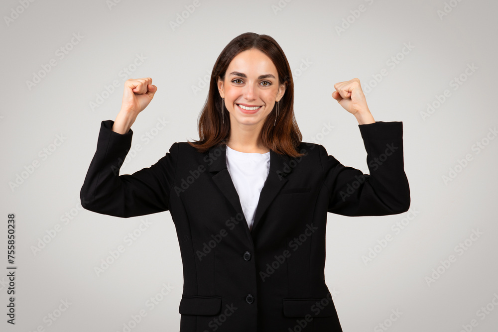 Joyful young businesswoman in a black suit with raised fists celebrates success Joyful young businesswoman in a black suit with raised fists celebrates success