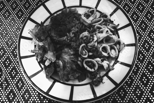 Gourmet dish at traditional French Basque country restaurant. Squids, rice with ratatouille, fresh green salad aesthetically served. Black white retro vintage graphic photo.