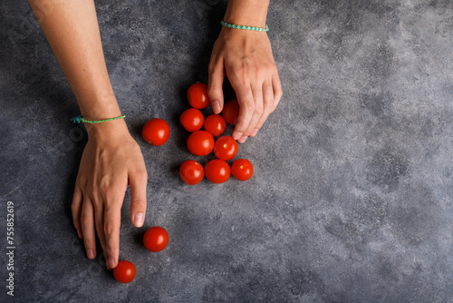 Woman hands with ripe tomatoes cherry on the gray table background, closeup. Handful of fresh red little tomatoes in female hands. Healthy snack and healthy eating, vegan and vegetarian food, top view