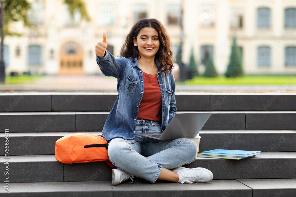 © Prostock-studio - Young eastern woman student using laptop outdoors, showing thumb up © Prostock-studio - Young eastern woman student using laptop outdoors, showing thumb up
