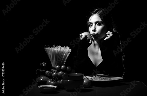 Hungry beautiful woman eat on noodles spaghetti on black background. photo