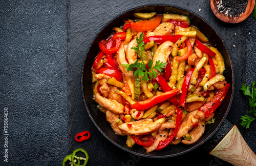 Stir fry turkey breast with red paprika and zucchini with sesame seeds, garlic, ginger and soy sauce in frying pan. Black table background, top view