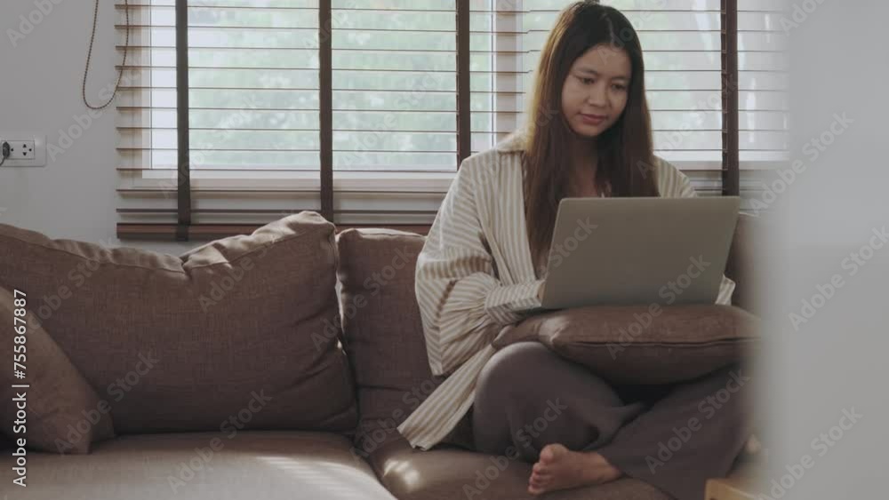 Asian woman sitting on sofa working from home using laptop Asian woman sitting on sofa working from home using laptop
