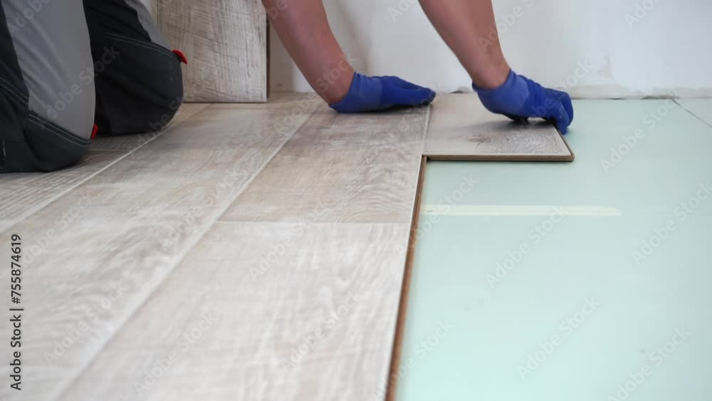 A man lays laminate flooring on the floor in a room. A man lays laminate flooring on the floor in a room.