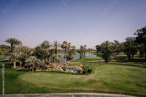 Agadir, Morocco - February 28, 2024- A scenic golf course with lush greenery, palm trees, a water feature, and clear skies. photo