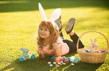 Child boy with easter eggs and bunny ears laying on grass painting eggs.
