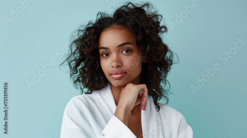 confident young woman with a subtle smile, posing with her hand on her chin against a blue background.