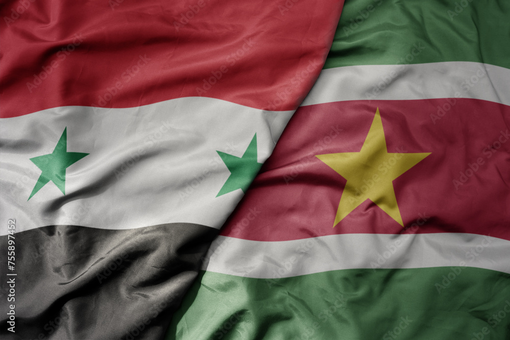 big waving national colorful flag of suriname and national flag of syria .