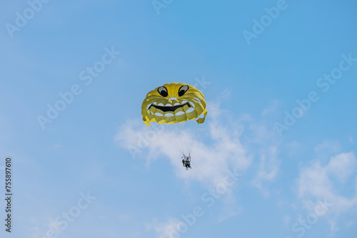 Yellow parasailing parachute on a blue sky background. A yellow parachute with a drawn smiley face © Armands photography
