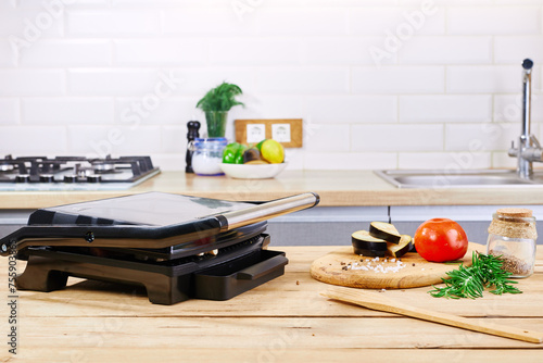 Electric grill with meat and spices on cutting board. Electric stove on modern kitchen.