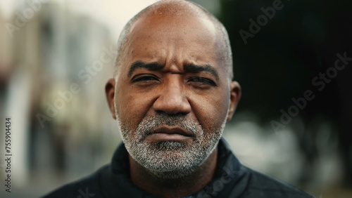 One serious mature black man standing outside in street during drizzle rain looking at camera with concerned expression. Middle-aged 50s person of African descent photo