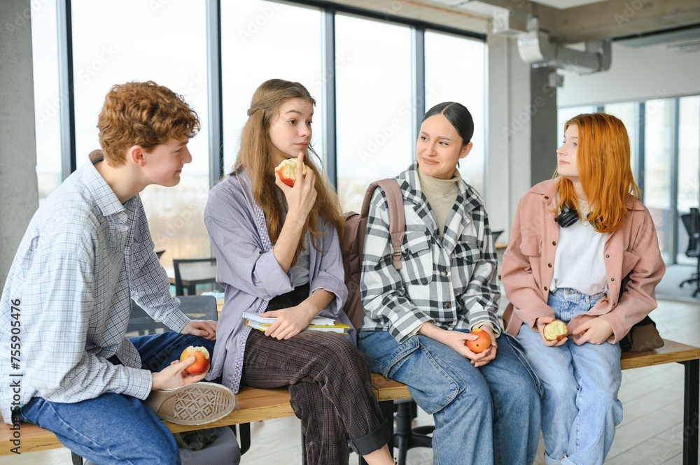 Cheerful students are sitting at desks and eating an apple during a break Cheerful students are sitting at desks and eating an apple during a break