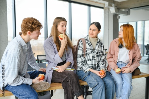 Cheerful students are sitting at desks and eating an apple during a break