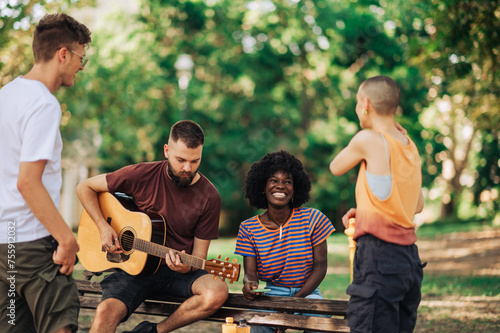 Four multiracial young adults are enjoying their time together and playing guitar.