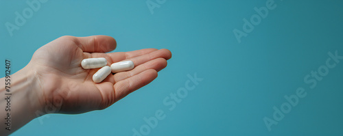 A hand holding three white capsules against a blue background. Medicines and pills concept banner. Treatment and addictions.